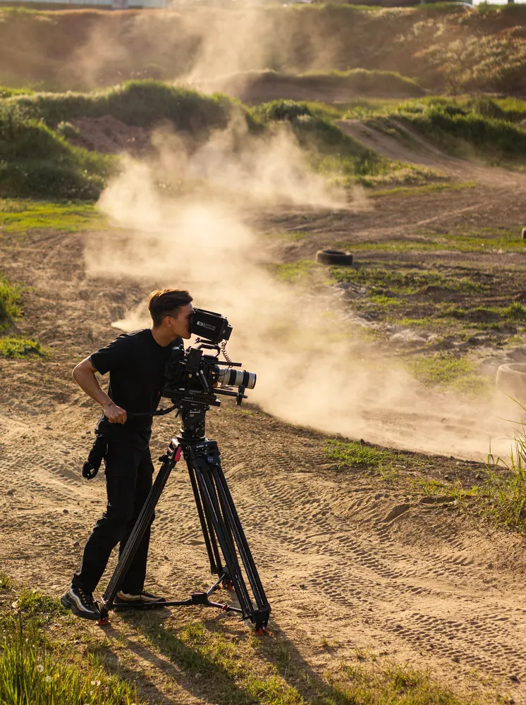 Videographer Oleksandr Stratiienko filming with a cinema camera on a dusty dirt track.