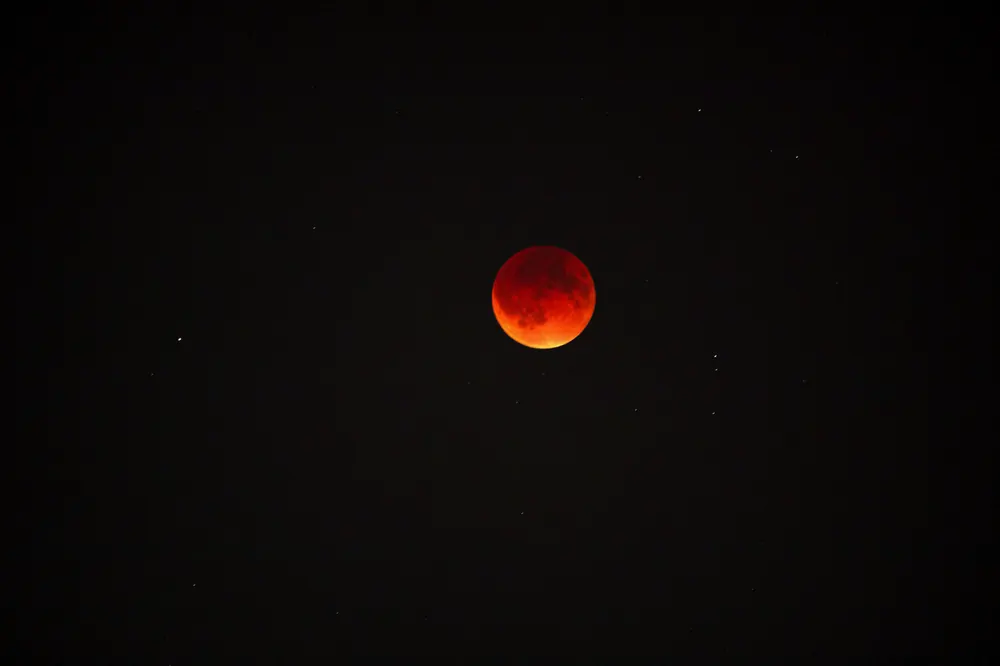 A blood moon during a total lunar eclipse against a dark starry sky.